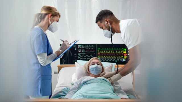 Ärzte und älterer Covid-19-infizierter Patient im Bett im Krankenhaus