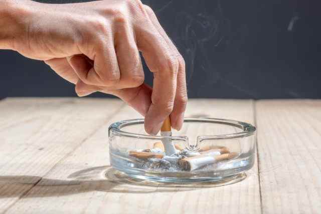 Hand drückte die Zigarette in einem transparenten Aschenbecher auf einem Holztisch aus
