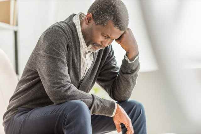 Selektiver Fokus eines depressiven afroamerikanischen Mannes, der mit gesenktem Kopf sitzt