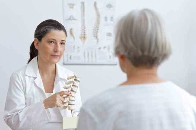 Orthopädie-Arzt zeigt älteren Patienten einen Bandscheibenvorfall an einem Wirbelsäulenmodell.
