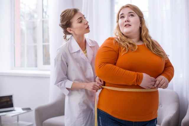 Arzt spricht mit einer fettleibigen Frau und misst sie.