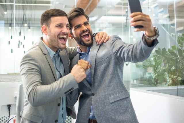 Zwei Männer in Geschäftskleidung machen ein Selfie-Foto im Büro
