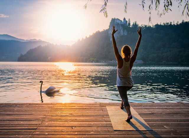 Frau am Seesteg, die Yoga-Übungen demonstriert, die unglaublich fitte Menschen tun