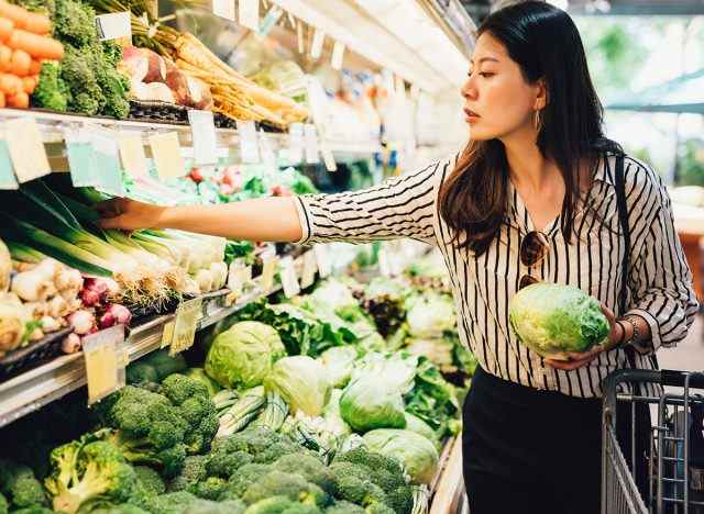 Frau hält Salat und greift nach mehr Produkten im Lebensmittelgeschäft