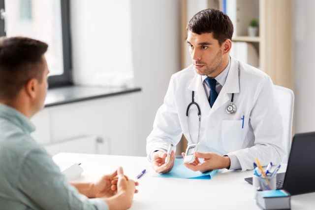 Arzt mit Glukometer und Insulinstift im Gespräch mit männlichen Patienten in der Arztpraxis im Krankenhaus