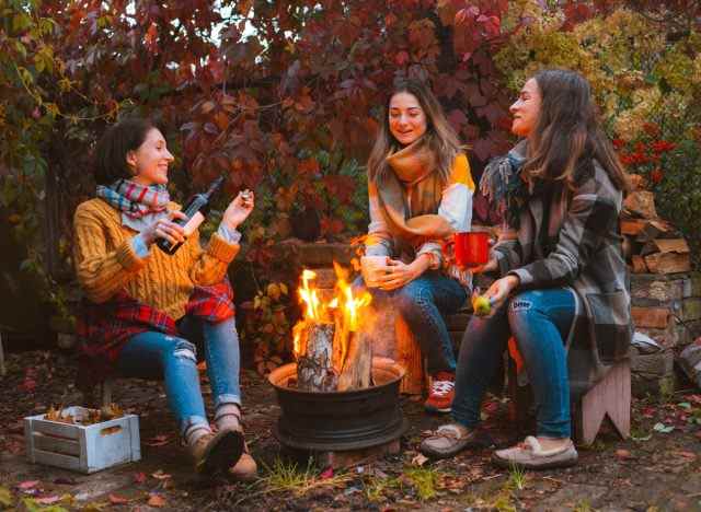 Reife Freundinnen trinken am Lagerfeuer auf einem Campingausflug im Herbst