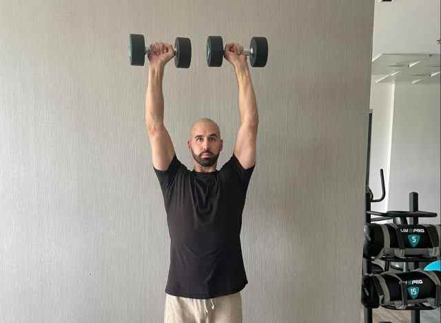 Trainer demonstriert Überkopfpresse als Teil des Trainings für stärkere Muskeln in Ihren 50ern