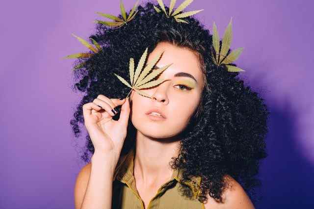 Porträt einer Frau mit Cannabisblatt in der Nähe ihres Gesichts