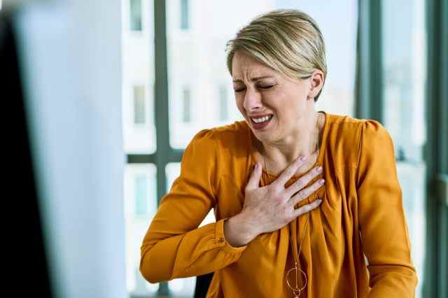 Geschäftsfrau, die Schmerzen in der Brust verspürt, während sie im Büro arbeitet.
