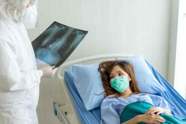 Patienten, die mit Maske auf einem Krankenhausbett liegen, während des Arztleseergebnisses einen Lungenröntgenfilm betrachten und eine Behandlung empfehlen