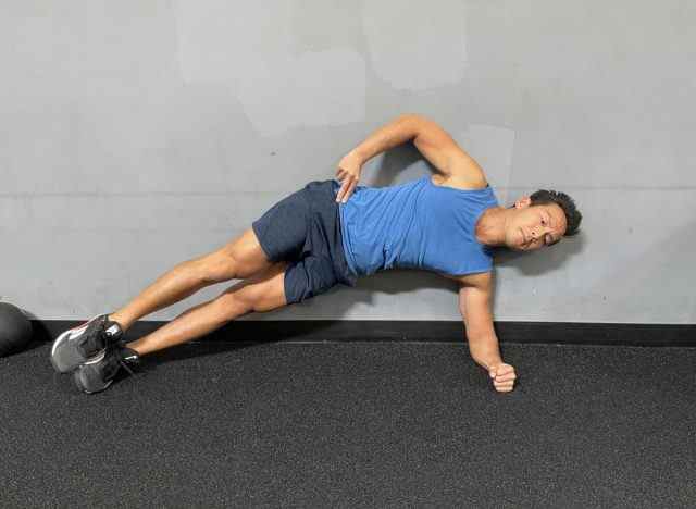 Trainer demonstriert Side Plank Hip Raise, um Muskelmasse nach 50 wiederzugewinnen