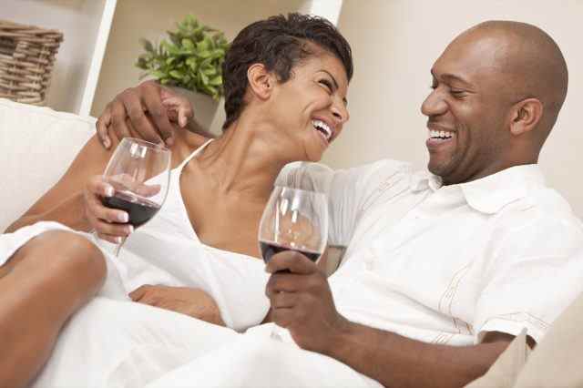 paar sitzt zu hause zusammen lachend und trinkt gläser rotwein