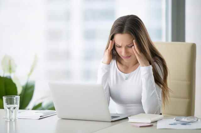 Junge frustrierte Frau, die am Schreibtisch vor Laptop arbeitet
