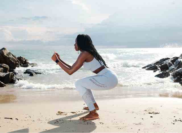 Frau am Strand, die tiefe Kniebeugen zur Gewichtsreduktion durchführt