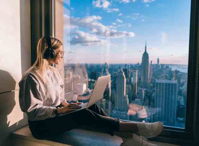 Frau mit Blick auf die Stadt, während sie braunes Rauschen hört und am Laptop arbeitet