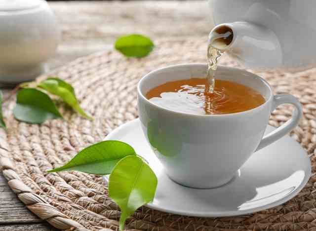 Gießen von grünem Tee in Teetasse