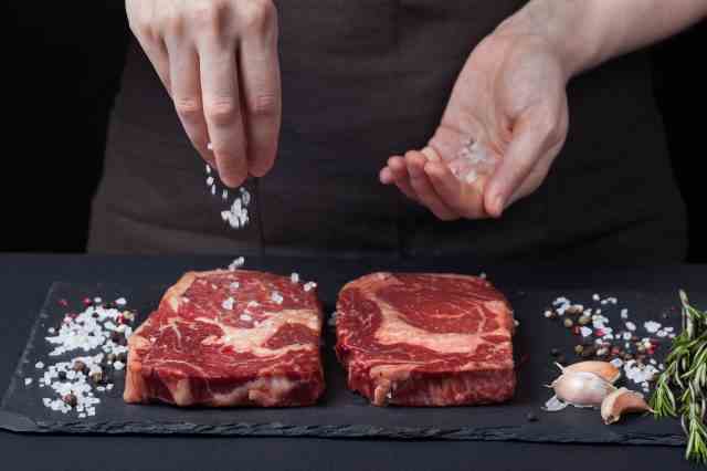 Koch streut Salz auf rohes Steak