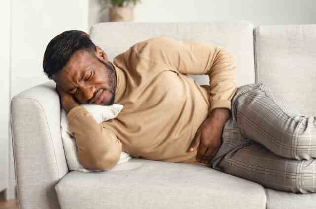 Leiden unter Bauchschmerzen, die den schmerzenden Magen berühren, der zu Hause auf der Couch liegt