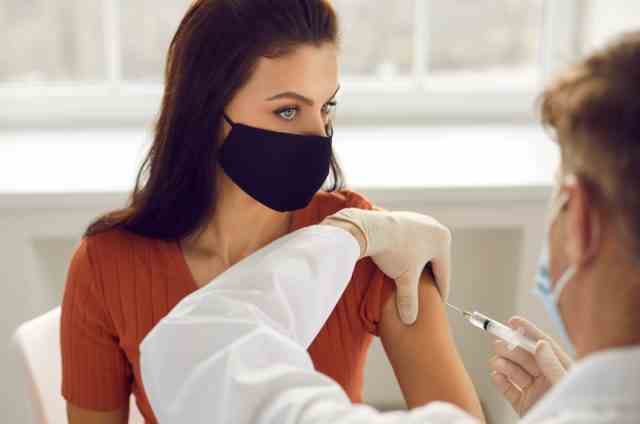 Frau in medizinischer Schutzmaske, die eine Injektion in die Armimpfung bekommt.