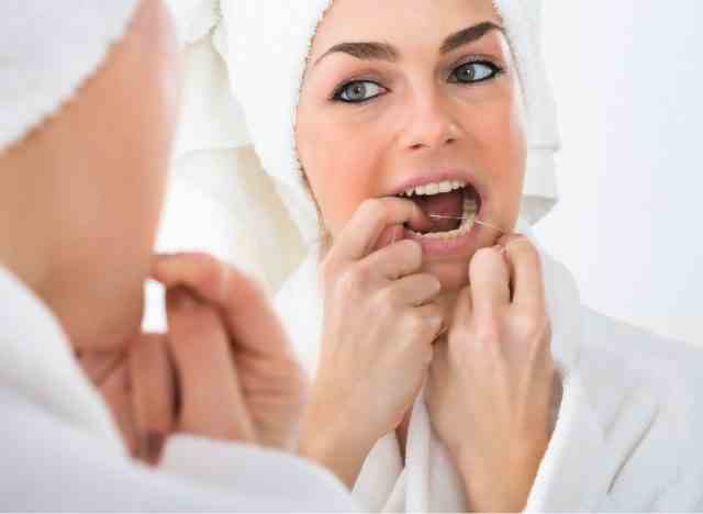 Frau, die ihre Zähne mit Zahnseide behandelt