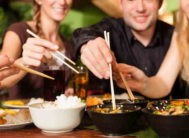 leute essen thailändisches und chinesisches essen mit stäbchen an einem tisch