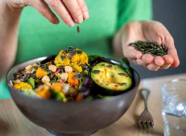 Frau Hinzufügen von Kürbiskernen zu einer Salatschüssel Gemüse Avocado pflanzliche Mahlzeit
