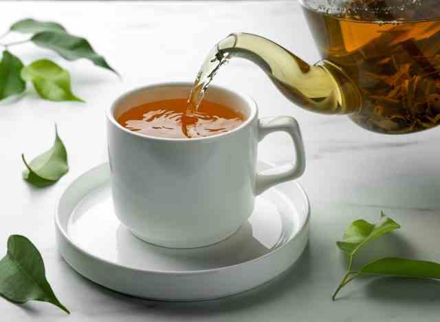 Gießen von grünem Tee in die Tasse