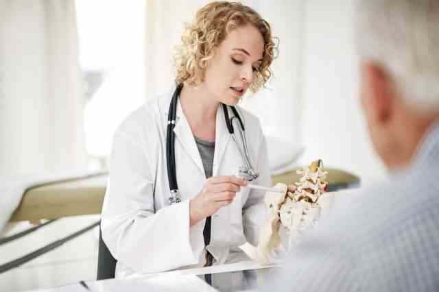 Aufnahme einer Ärztin, die einer älteren Patientin in ihrem Büro ein medizinisches Verfahren anhand eines Modells erklärt
