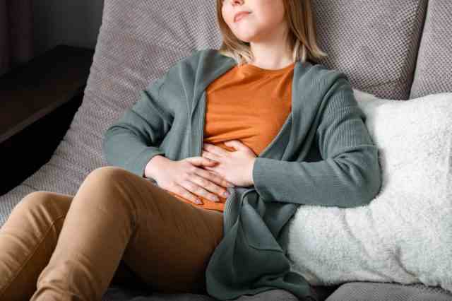 Junge Frau leidet, windet sich vor Bauchschmerzen und liegt auf der Couch im Wohnzimmer zu Hause