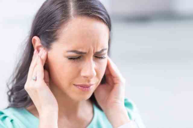 Junge Frau hat Kopfschmerzen, Migräne, Stress oder Tinnitus - Geräusche, die in ihren Ohren pfeifen.