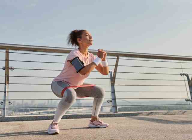 Reife Frau, die Kniebeugen auf der Brücke durchführt und Fitnessgewohnheiten demonstriert, die Muskelermüdung verursachen