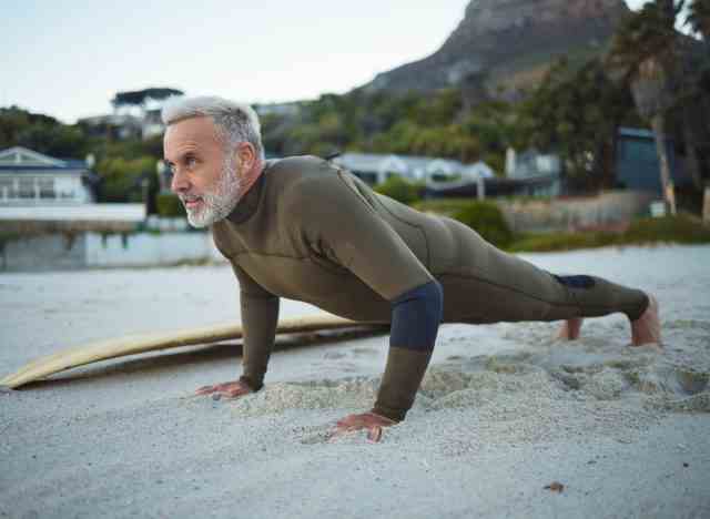 Reifer Mann macht Strand-Liegestütze Muskelausdauerübungen in einem Neoprenanzug