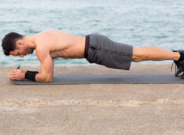 Mann macht Unterarmplanke auf Yogamatte am Wasser, Konzept der Körpergewichtsübungen, um das Gewicht niedrig zu halten