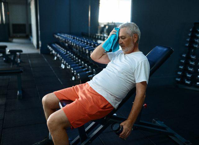 älterer Mann sitzt während des Trainings müde auf der Trainingsbank