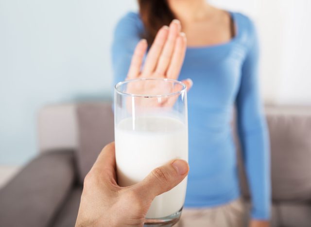 Frau, die eine ausgestreckte Hand hochhält und einem Mann nein sagt, der ihr ein Glas Milch anbietet