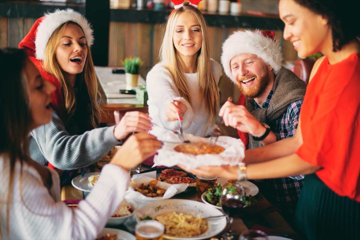 Gruppe von 20- oder 30-Jährigen, die gemeinsam mit Weihnachtsmützen ein Feiertagsessen essen