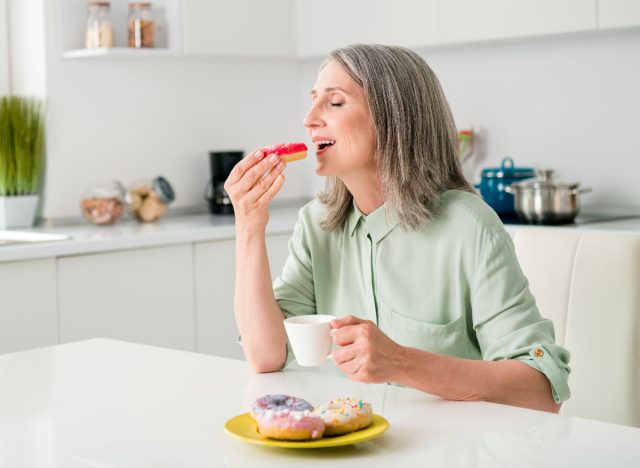 Reife Frau isst Donut, ungesunde Lebensgewohnheiten, die Ihren Rücken zerstören