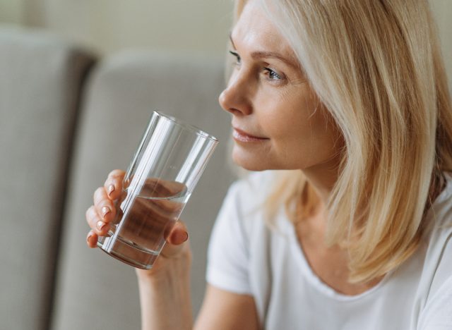 Reife Frau trinkt zu Hause ein Glas Wasser