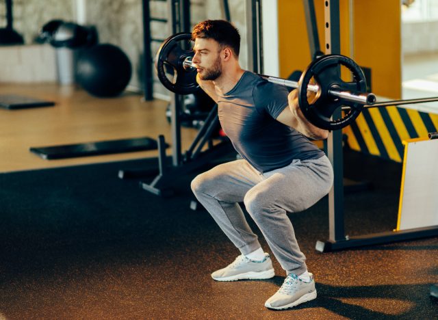 Fitter Mann, der Langhantelkniebeugen im Fitnessstudio durchführt, Konzept von Kraftübungen für Männer
