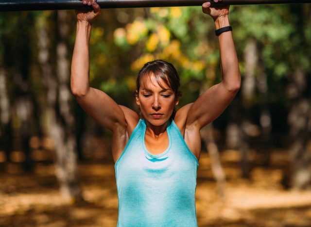 Muskulöse Frau macht Klimmzüge im Freien, Konzept von Übungen, um hängendes Bauchfett in Ihren 40ern zu schmelzen