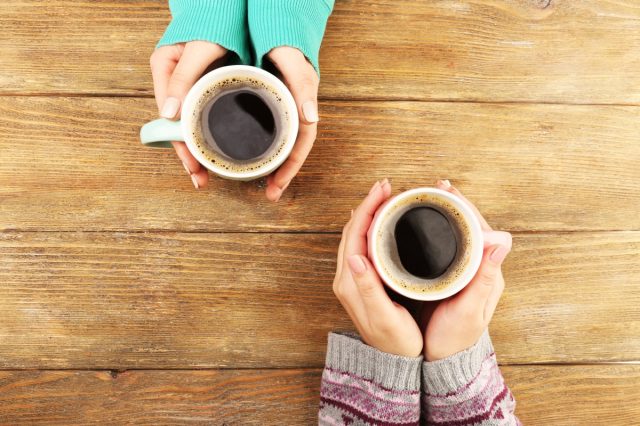 Frauenhände halten Tassen Kaffee auf rustikalem Holztisch 