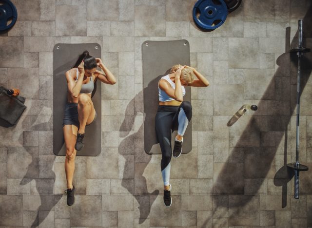 two women doing bicycle crunches during ab workout on floor