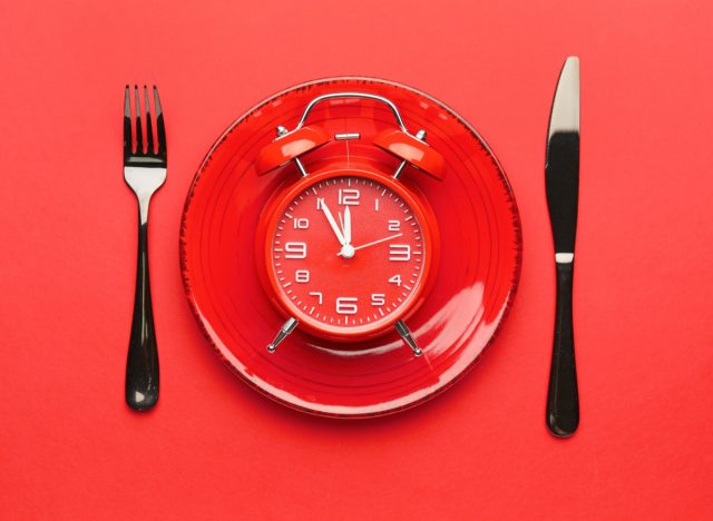 Uhr auf Teller mit Gabel und Messer, Konzept des intermittierenden Fastens