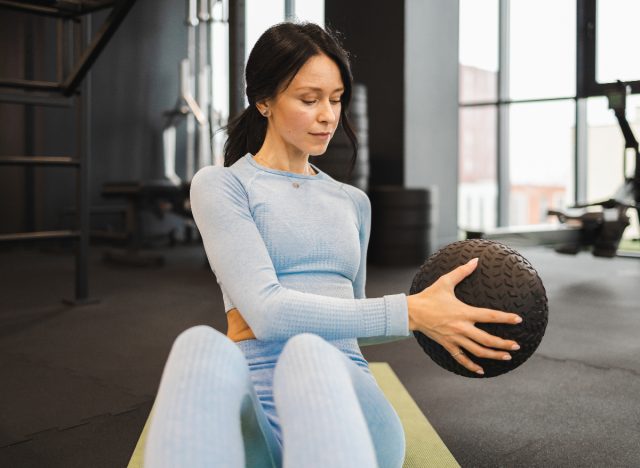 Frau macht russische Drehungen mit Medizinball, Konzept von Übungen für einen schlankeren Rumpf in 30 Tagen