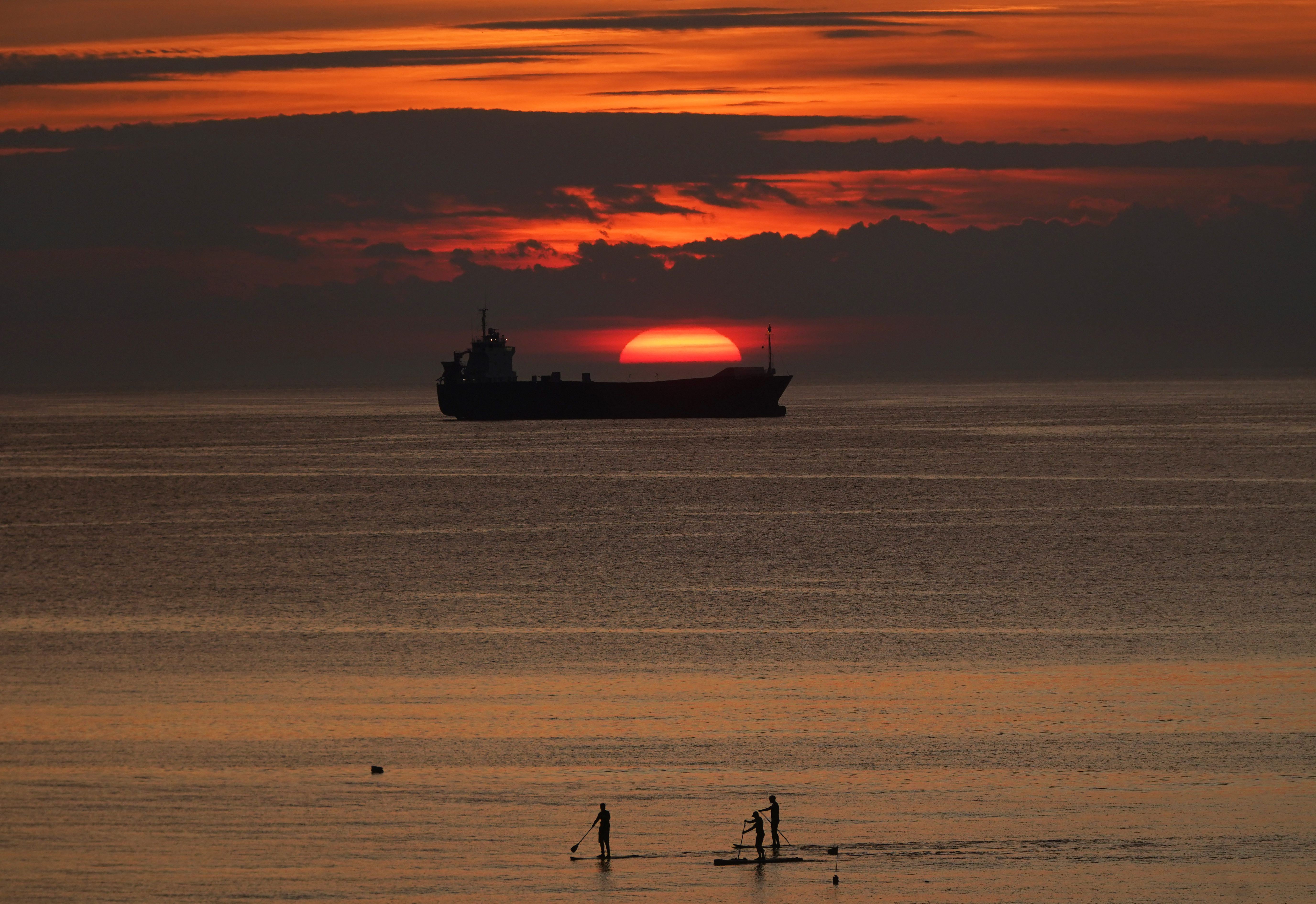 Paddle-Boarder starten heute früh, wenn die Sonne über einem Frachtschiff in der Nähe von Cullercoats Bay auf North Tyneside aufgeht