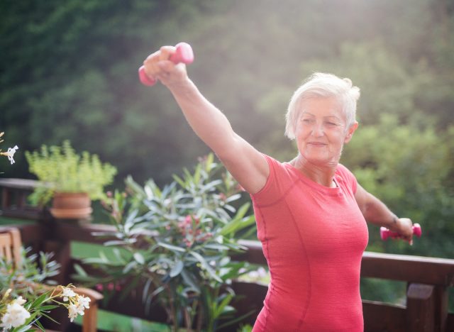 Ältere Frau hält Hanteln und trainiert draußen auf ihrem Deck