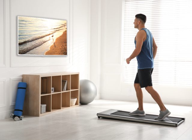 Mann macht zu Hause einfache Cardio-Übungen auf dem Laufband, während er fernsieht