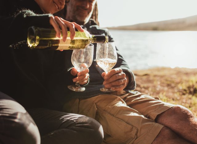 Älteres Paar schenkt Wein im Freien am See ein, Konzept der schlechtesten Gewohnheiten für die Gesundheit des Gehirns