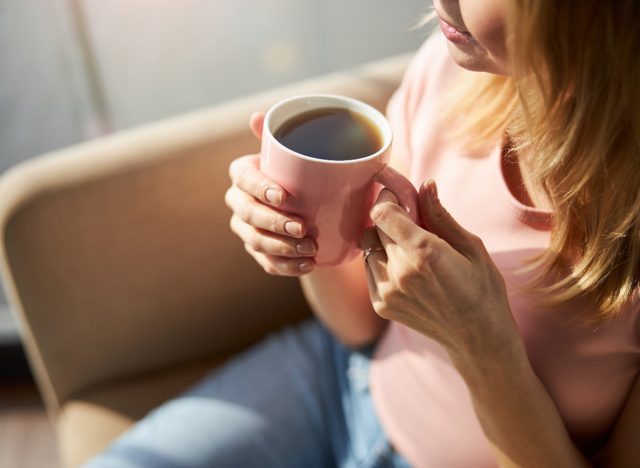 Nahaufnahme einer reifen Frau in rosa Hemd mit einer rosa Tasse Kaffee, Konzept, wie Kaffeetrinken Ihnen beim Abnehmen helfen kann