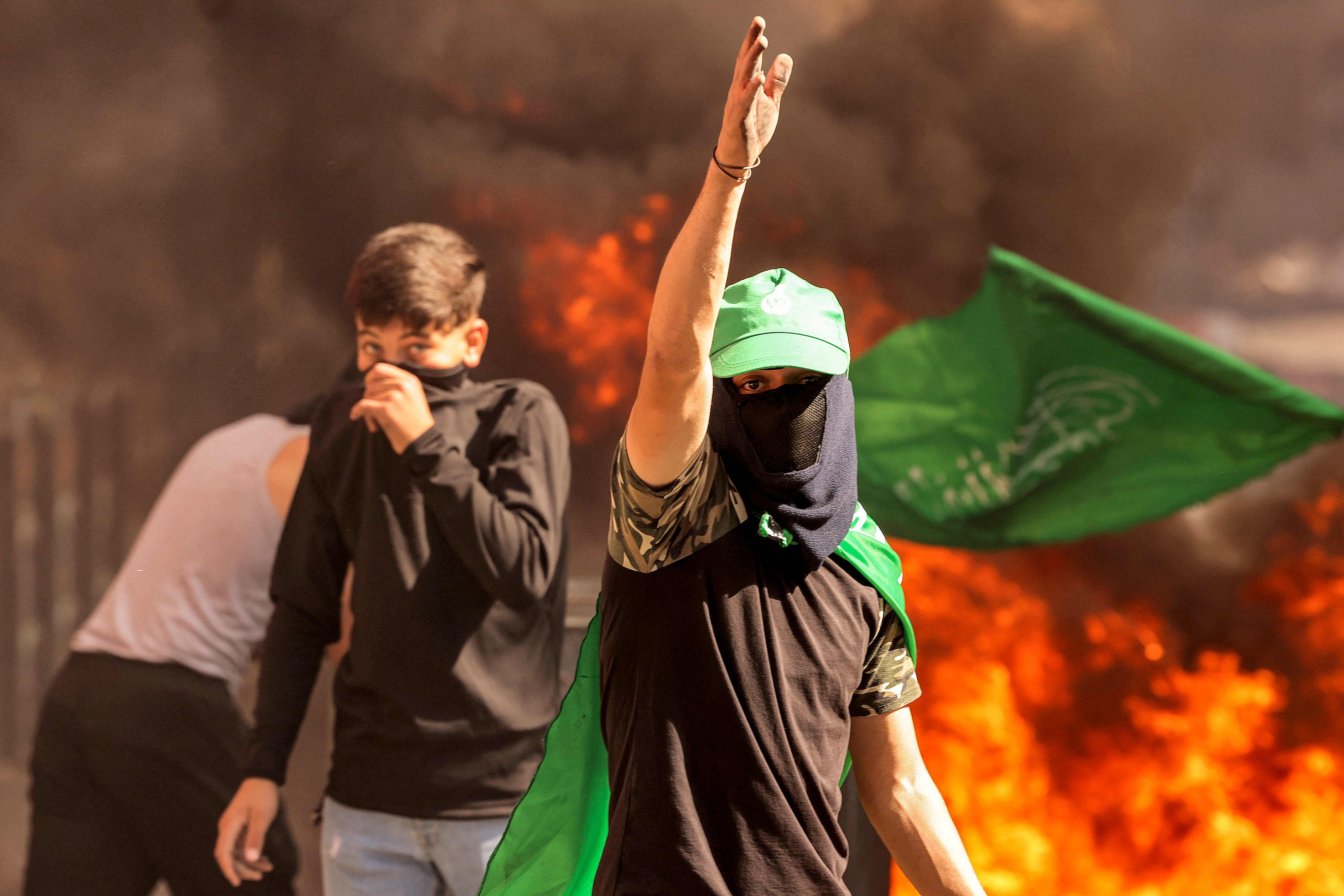 Ein maskierter palästinensischer Demonstrant gestikuliert, während er in der Westbank in der Nähe brennender Reifen geht